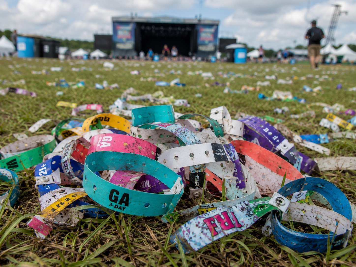 Discarded plastic wristbands piled on festival grass, highlighting the environmental waste generated by single-use event credentials.